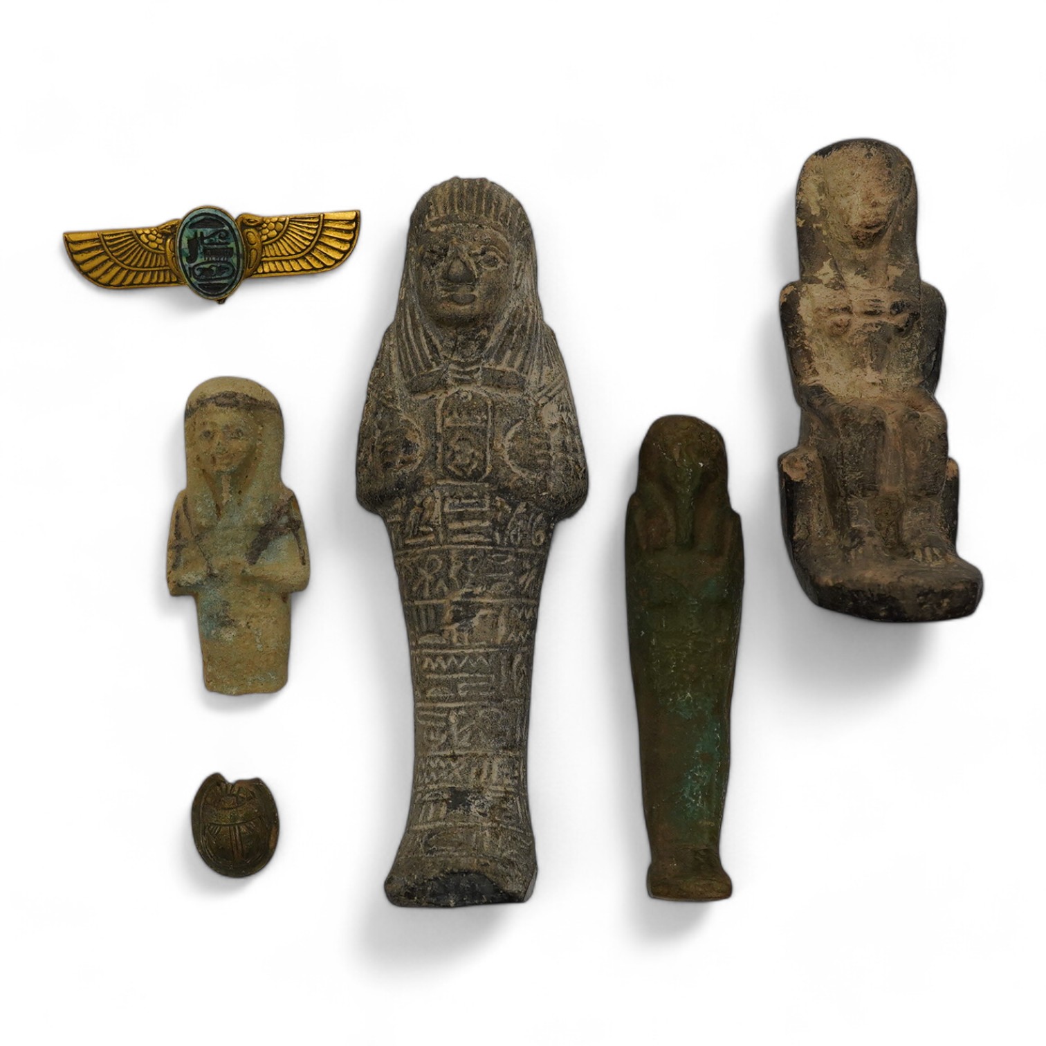 Three ancient Egyptian carved stone ushabti, tallest 15cm, with carved hieroglyphs to the body, together with a seated figure, possibly of Isis, a scarab and a yellow metal brooch with inset stone carved with hieroglyphs